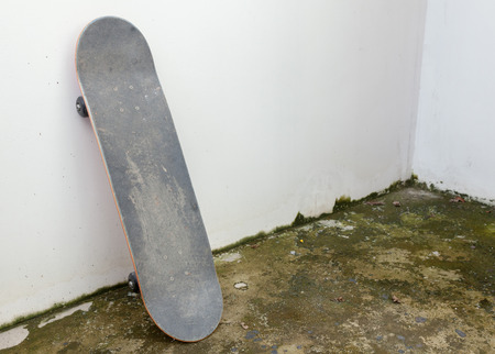 skateboard leaning against white concrete wall and dirty floorの写真素材