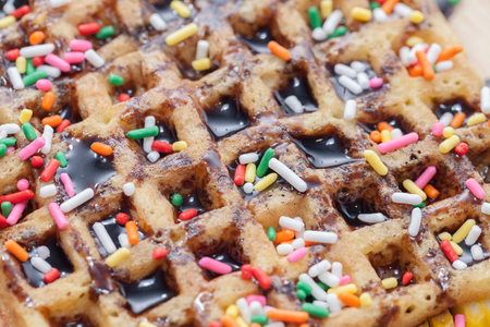 Waffles with melted chocolate and colorful sparkle on wooden plateの写真素材