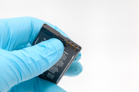 hand in blue glove holding mobile battery on white background