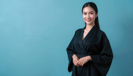 A young Asian woman with straight dark hair, in a black robe kimono, stands in a modern glass buildingの素材