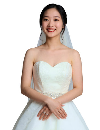 A smiling Asian bride with dark hair in an updo, wearing a strapless white wedding dress, and veil, against a white background.の素材