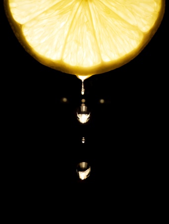 cut of lemon with falling drop on dark background の写真素材