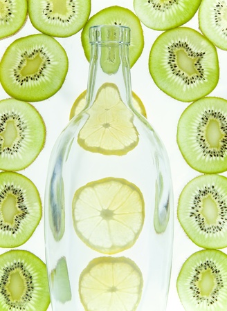 Bottle with cut lemon and kiwi fruit on white backgroundの写真素材