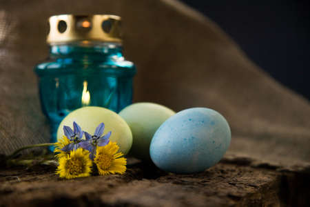 Blue and green easter eggs with blue light candle with yellow and blue flowers on wooden table and...