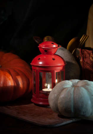 Autumn still life with red candle lantern and pumpkins on wooden kitchen table in the darknessの写真素材