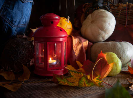 Autumn still life with red candle lantern, autumn maple leaves and pumpkins on wooden tableの写真素材