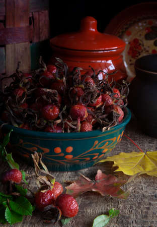 Autumn stilllife with fresh rosehips in green clay plate on wooden table with rustic kitchen potsの写真素材