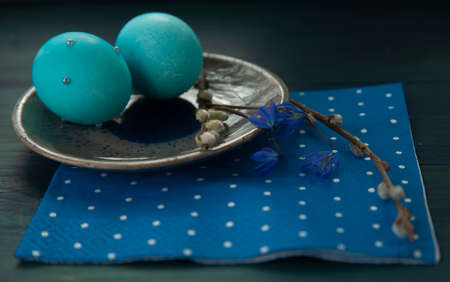 easter table setting with blue eggs, blue napkin, blue spring flowers and willow branchの写真素材