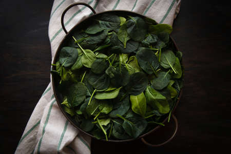 Fresh spinach leaves in metal bowl on dark wooden table, low key, top view,の写真素材