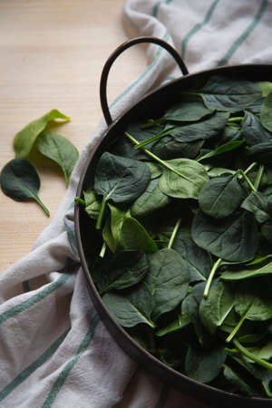 Fresh spinach leaves in metal bowl on white wooden table, top view, close up