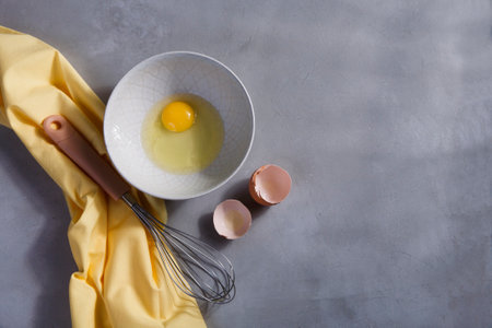 A bowl with yolk and a whisk on gray kitchen table with yellow cloth, copy spaceの写真素材