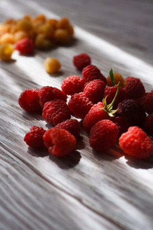 Two handfuls of fresh red and yellow raspberry on white wooden table.