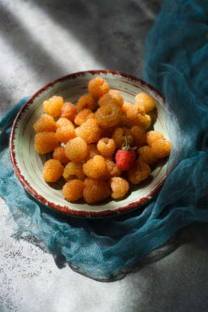 Yellow raspberry on green plate and green table with blue cloth.