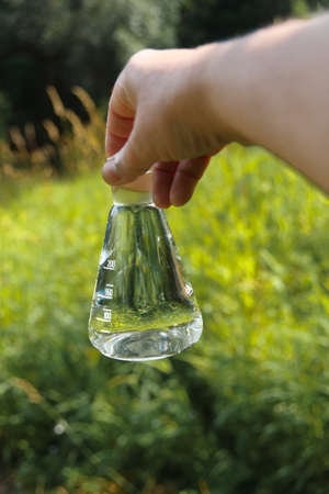 A hand holding the chemical flask with spring water with a natural landscape in the background.