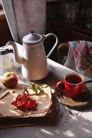 Still life in old rustic kitchen with a cup of tea and a bunch of red rowan and red apples, autumn morning tea concept.の写真素材