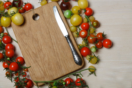 Little red, yellow, green and black cherry tomatoes on white table with wooden cutting board in the middle, place for text, flat lay.の写真素材