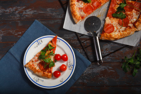 Fresh made traditional pepperoni pizza on blue wooden table with a slice of pizza on white plate with cherry tomatoes.の写真素材
