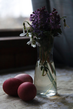 Snow drops and fumewort in glass vase with painted red eggs on rustic table, Easter selebration concept, selective focus.の写真素材
