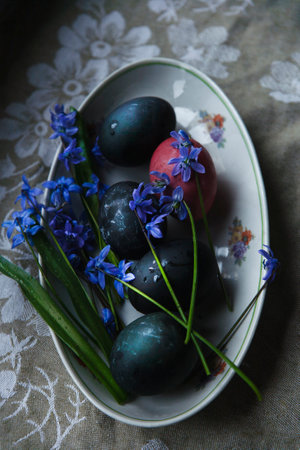 Happy Easter! Easter naturally painted dark blue and pink eggs on plate with blue bluebell flowers on rustic table, top view, selective focus, low key.の写真素材