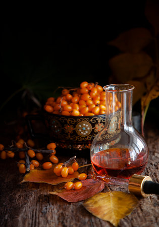 Sea-buckthorn oil in chemical flask with berries in a cup, low key, selective focus