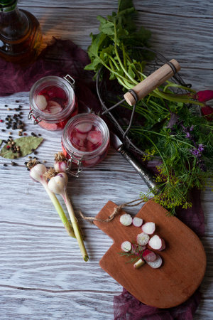 Two Glass Jars with Pickled Radish with greenery, garlic and spices on white wooden table, flat layの写真素材