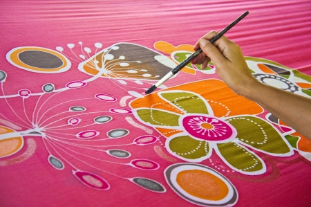 An artist carefully paint the floral/flower motif on a red silk batik fabricの写真素材