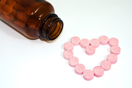 Red color pills spill out a glass medicine bottle in a heart shape on white backgroundの写真素材