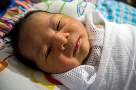 Close up of a newborn Asian infant sleeping in bed 