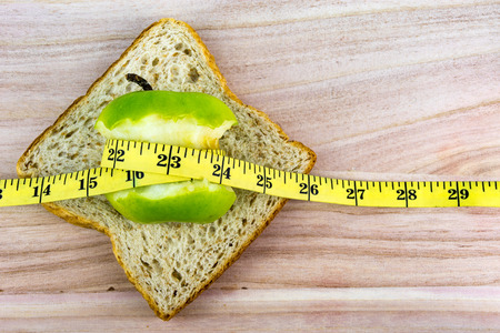 Apple on top of bread wrapped with measuring tape on wooden surface. Healthy diet concept. Selective...