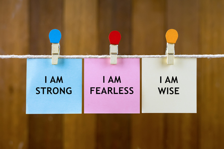 Word quotes of I AM STRONG, I AM FEARLESS, I AM WISE on colorful sticky papers hanging by a rope against blurred wooden background.の写真素材