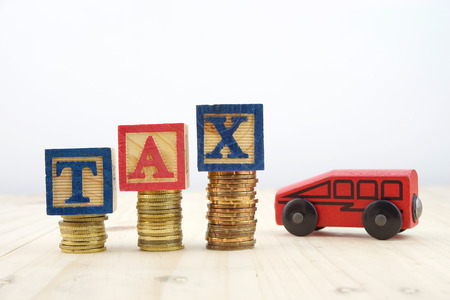 TAX concept with wooden blocks on stacked of coins with toy car against white backgroundの写真素材