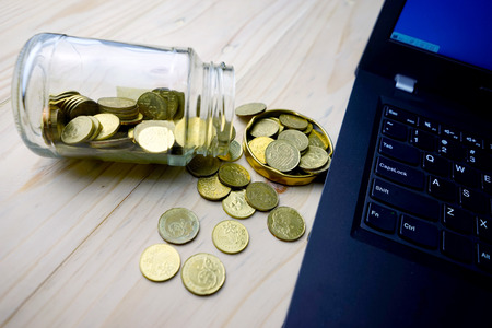 Financing concept. Golden coins with glass container and laptop on the table.Selective focusing.の写真素材