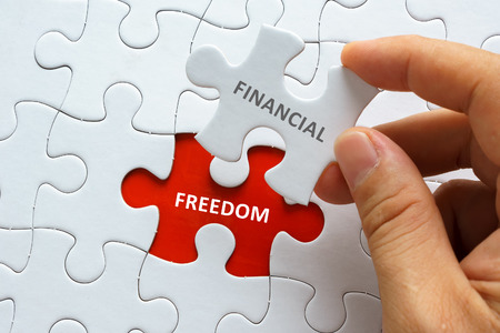 Hand holding piece of blank jigsaw puzzle with word FINANCIAL FREEDOM.の写真素材