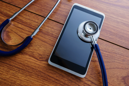 Conceptual image of a smartphone being diagnosed with a stethoscope on wooden background.の写真素材