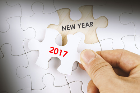 Hand holding a piece of jigsaw puzzle with word NEW YEAR 2017.