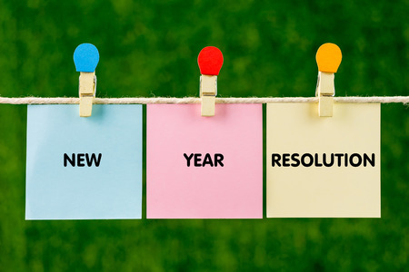Sticky color papers with word NEW YEAR RESOLUTION hanging against green background.の写真素材
