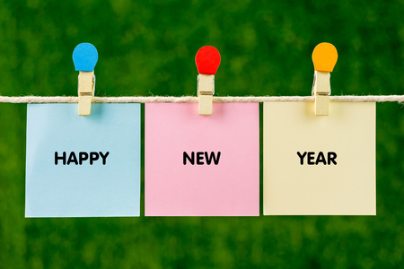 Sticky color papers with word HAPPY NEW YEAR hanging against green background.の写真素材
