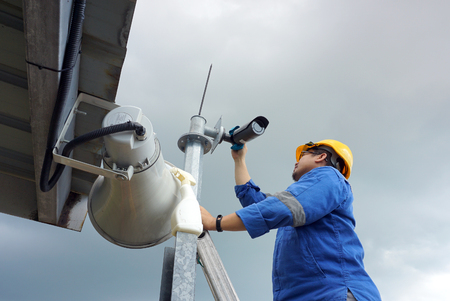 A male worker doing a maintenance work by cleaning and inspecting security camera.の写真素材