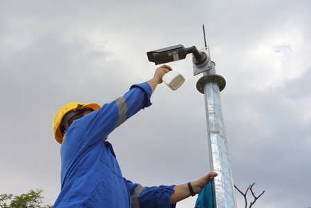 A male worker doing a maintenance work by cleaning and inspecting security camera.の写真素材