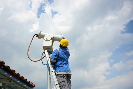 A male worker doing a maintenance work by cleaning and inspecting security camera.の写真素材
