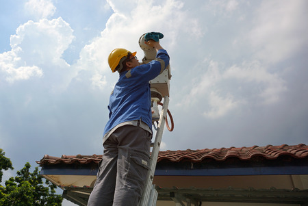 A male worker doing a maintenance work by cleaning and inspecting security camera.の写真素材