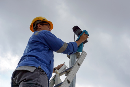 A male worker doing a maintenance work by cleaning and inspecting security camera.の写真素材