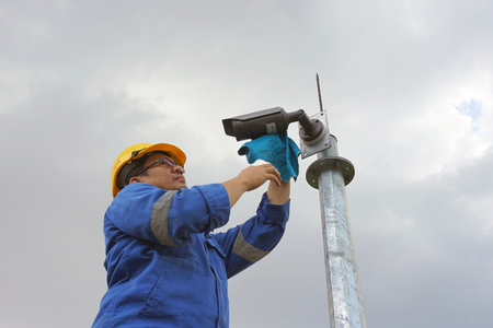 A male worker doing a maintenance work by cleaning and inspecting security camera.の写真素材