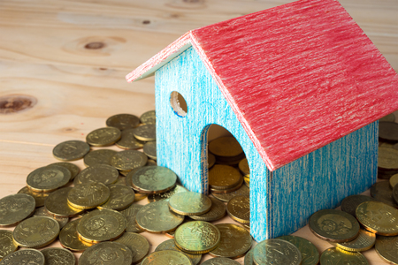 Conceptual image of small house with gold coins on wooden surface. Selective focus.の写真素材