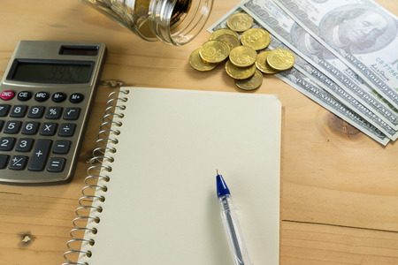 Conceptual image of notepad, money and calculator on wooden table. Selective focus.の写真素材