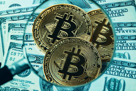 Close-up shot of golden bitcoin cryptocurrency through a magnifying glass on top of US dollar billsの写真素材