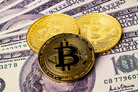 Close-up shot of golden bitcoin cryptocurrency on top of us dollar billsの写真素材