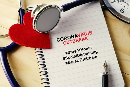 Conceptual image. Stethoscope with heart shape, notepad, clock and pen on wooden table with coronavirus outbreak hashtag campaign.の写真素材