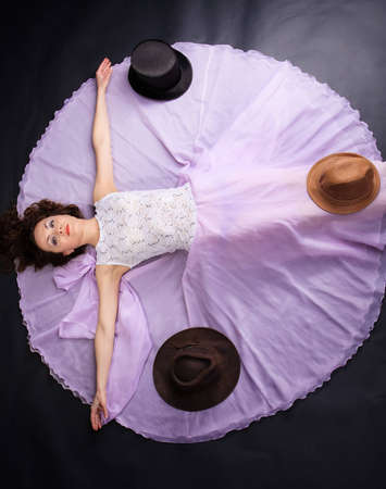 Attractive woman lying on the floor in liliac dress with a three hatsの写真素材