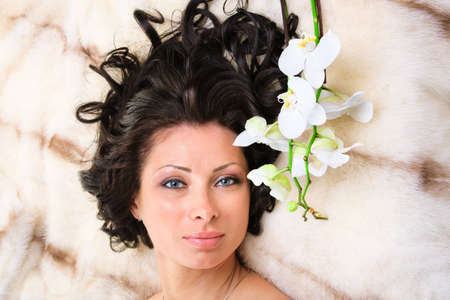 Young beautiful woman with flower lies on fur coatの写真素材